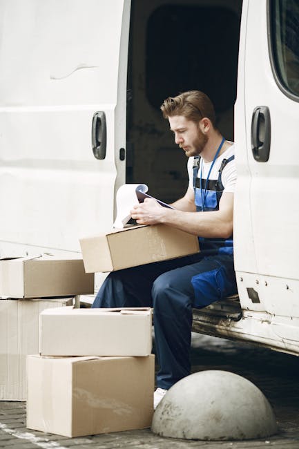 Inside a white delivery van used for home relocation, four large cardboard boxes with white shipping labels are stacked, with three positioned on the van's floor and one placed on top of the others. The boxes are sealed with packing tape, and the van's interior ceiling and side panel are visible, with the rear door open to reveal an outside pavement and a partial view of a vehicle in the background. This scene depicts the loading process common in furniture transport and packing during a house removal, with the boxes prepared for transport by Man and Van Knightsbridge, supporting efficient relocation services in Knightsbridge. The environment is brightly lit, with existing moving equipment like trolleys or straps not visible, emphasizing a straightforward loading operation for furniture and packed goods.